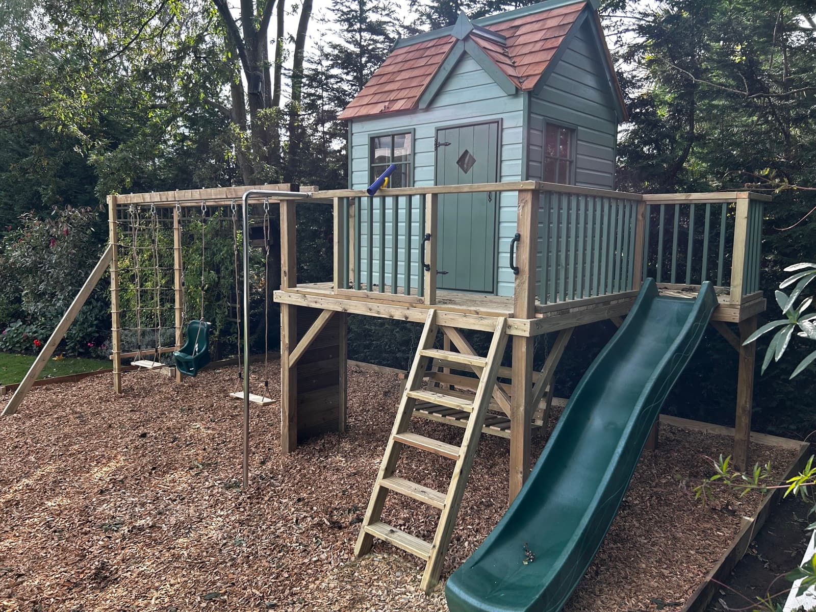 A Damson Playhouse: the ply-lined and painted Damson cottage with cedar shingle roof, on a full play deck with wave slide and swings