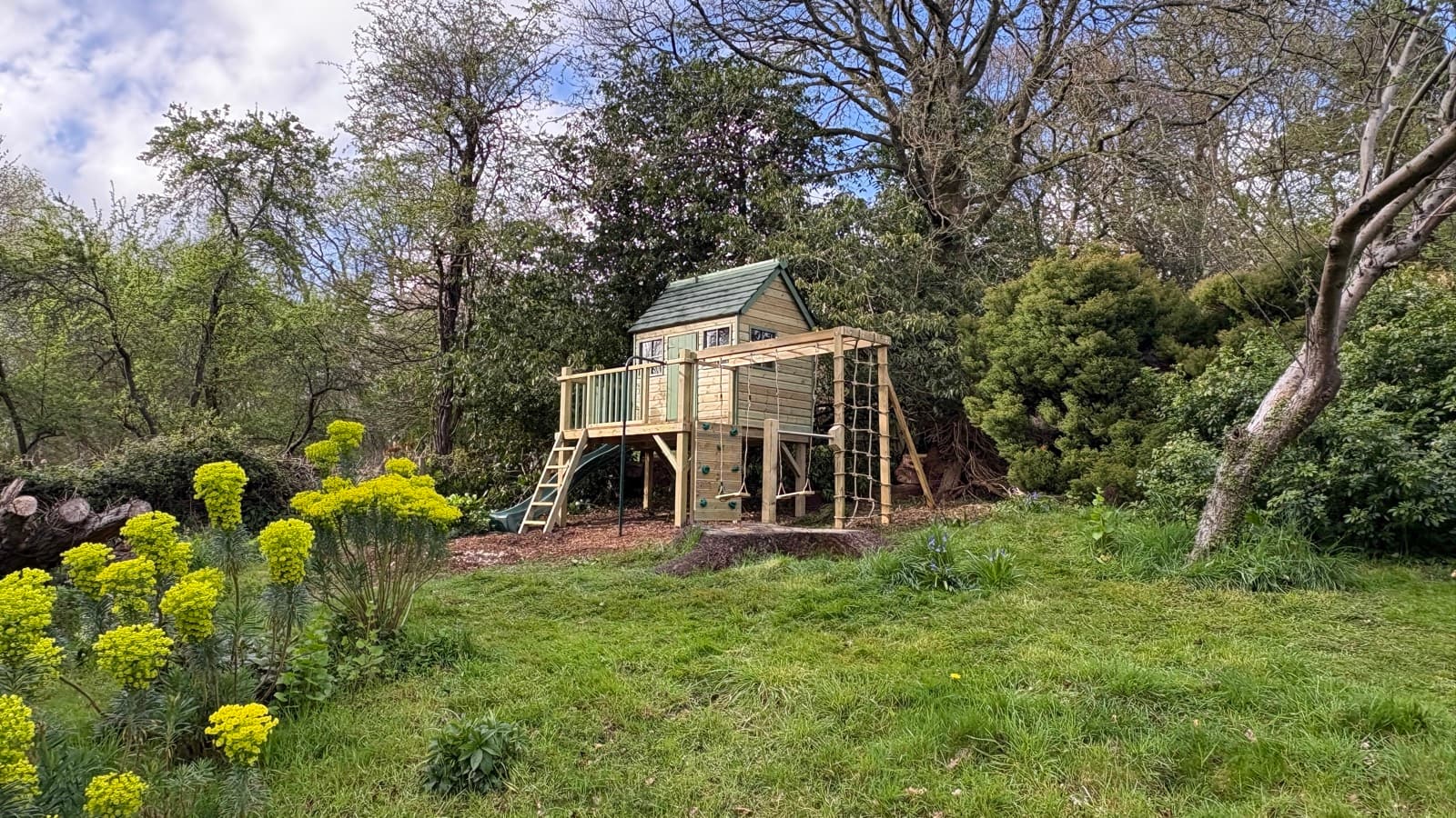 A Forest Playhouse on its full-width play deck, with a wave slide, monkey bars, climbing wall and double swings