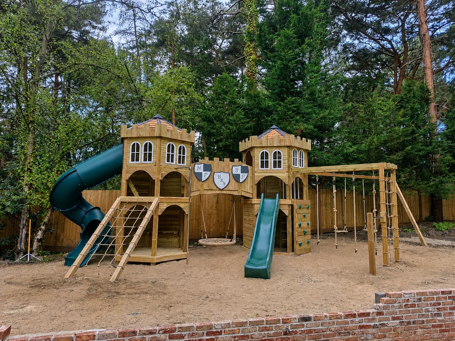 The play castle at Poole: twin battlemented hex towers joined by a bridge with monogrammed shields, nest swing at its centre