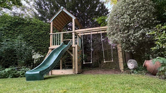 A Treetops Tower: a single roofed timber tower with a green wave slide, double swings and climbing steps on a lawn