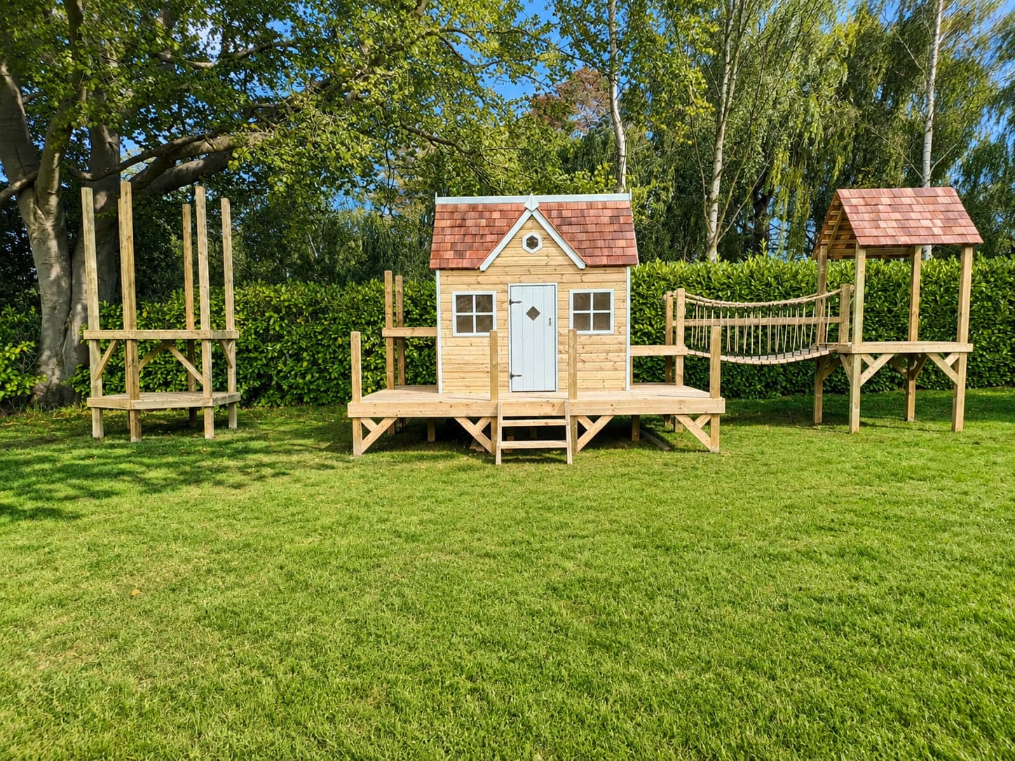 A Forest estate mid-extension: a bare tower frame stands ready beside the finished playhouse and bridge
