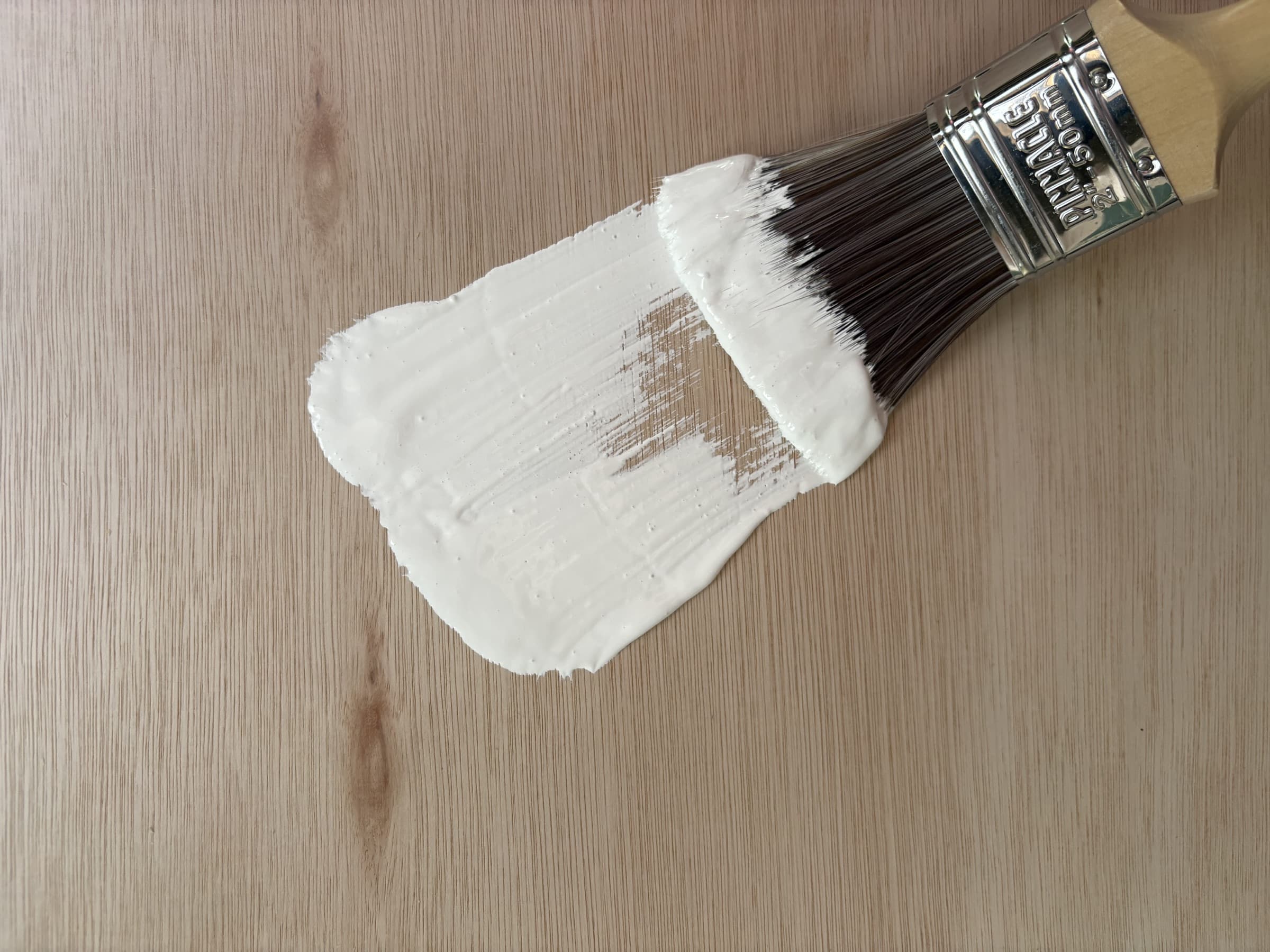 A brush drawing white paint across timber for the hand-painted Real House finish